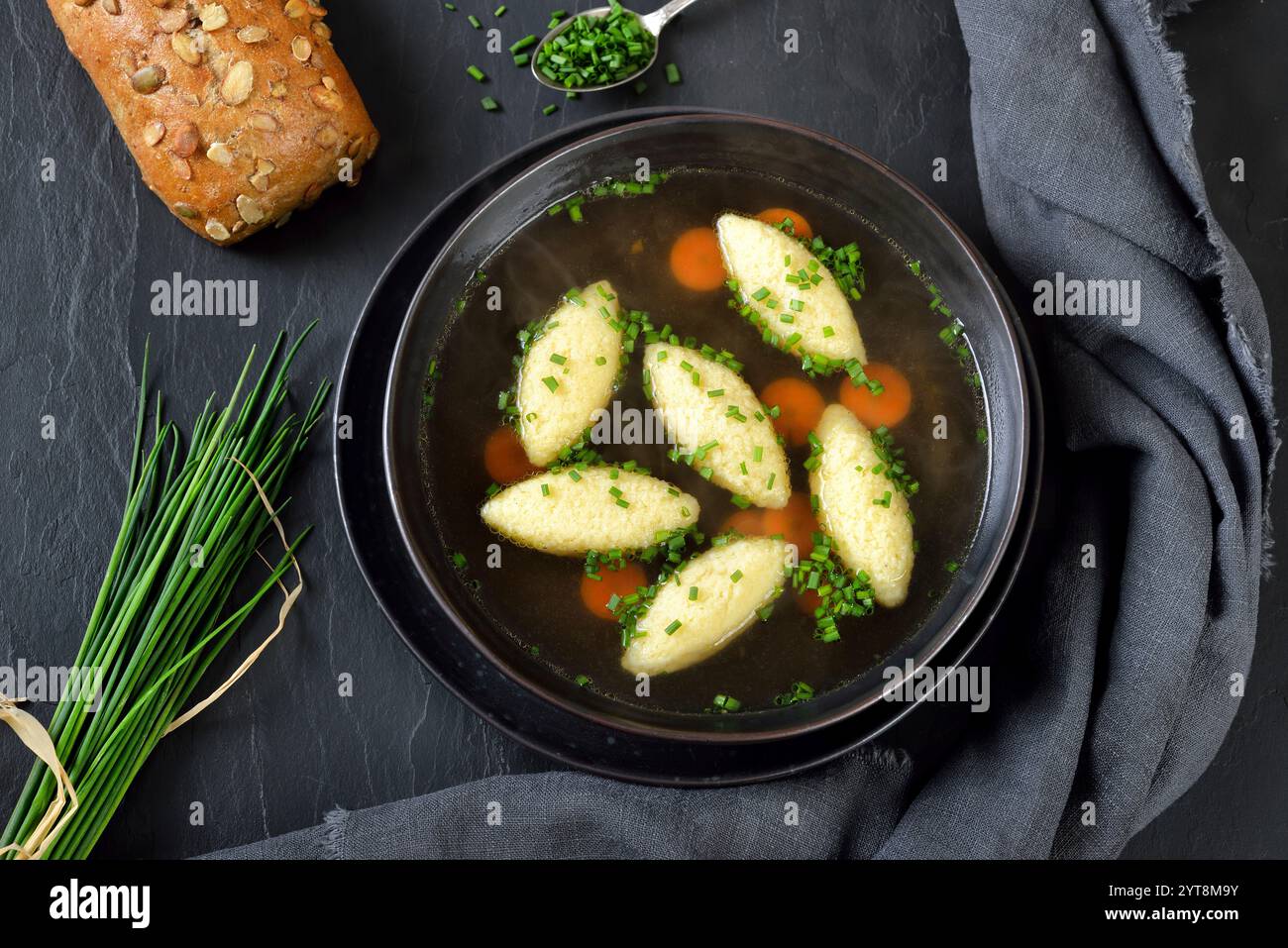 Abbondante zuppa di gnocchi di semola servita su un piatto di ardesia con un rotolo di semi di zucca Foto Stock