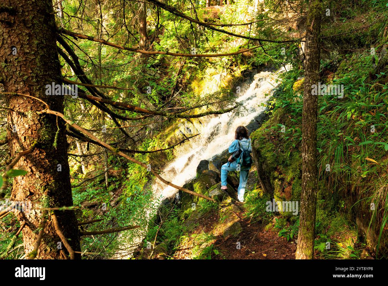 Una donna si trova ai margini di una cascata e ammira l'acqua che cade Foto Stock Una donna si trova ai margini di una cascata e ammira l'acqua che cade Foto Stock