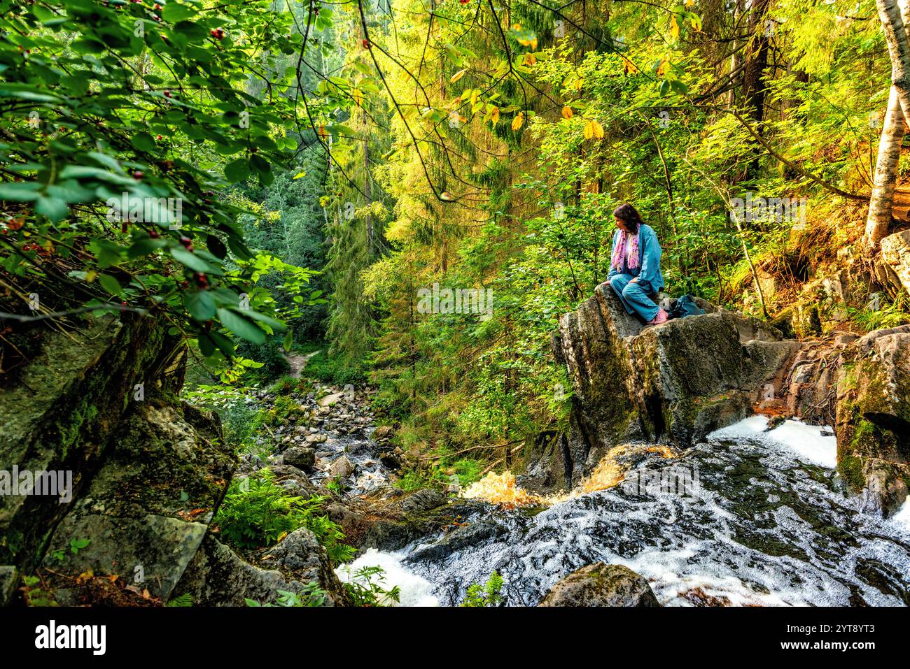 una donna siede su una roccia ai margini di una cascata e guarda in basso Foto Stock una donna siede su una roccia ai margini di una cascata e guarda in basso Foto Stock