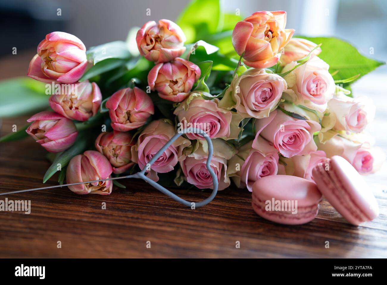 Bellissimo bouquet di fiori con dolci prelibatezze. A forma di cuore, dolci dolci con rose rosa e tulipani sul tavolo di legno. Sfondo per il giorno della mamma e il matrimonio. Foto Stock