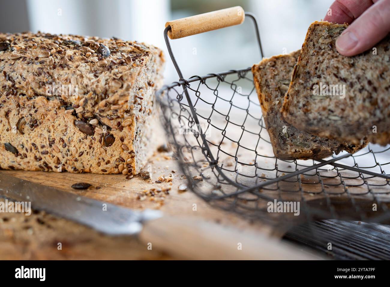 Una mano prende dal cestino pane multigrano appena tagliato. Primo piano di fronte alla finestra luminosa. Foto Stock