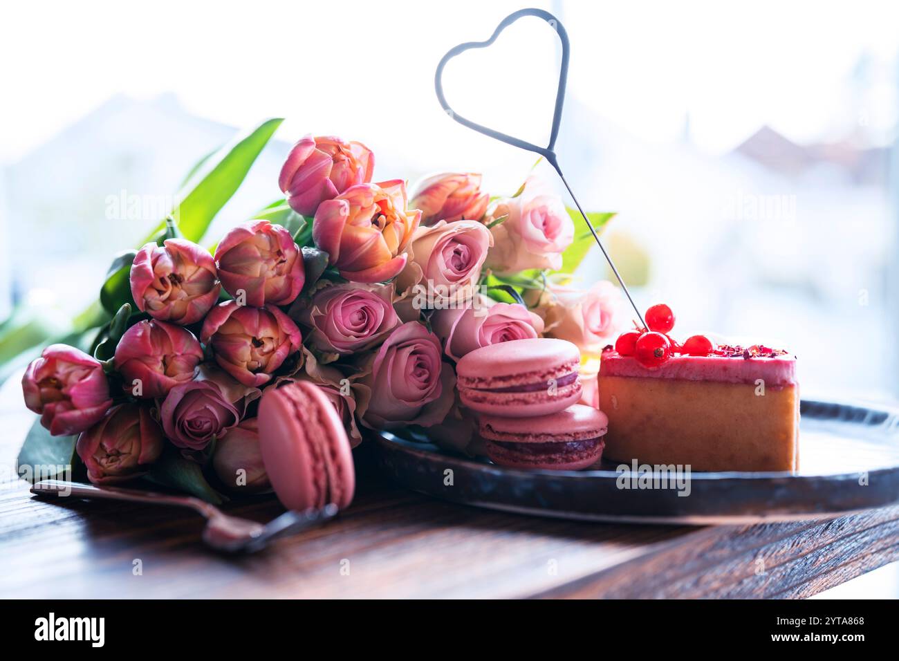 Bellissimo bouquet di fiori con dolci prelibatezze. A forma di cuore, dolci dolci con rose rosa e tulipani sul tavolo di legno. Sfondo per il giorno della mamma e il matrimonio. Foto Stock