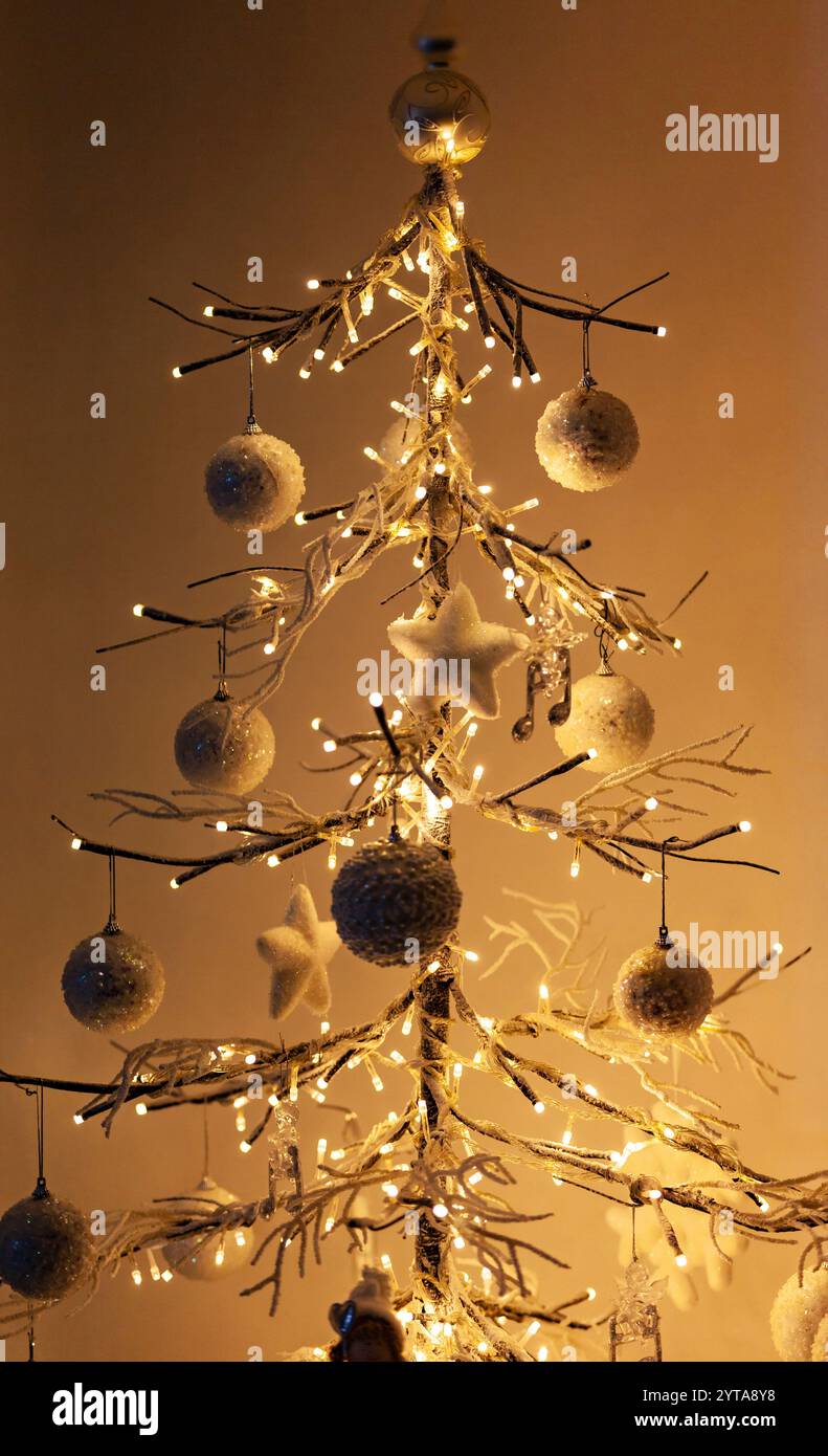 Il minimo albero di Natale in piedi di fronte a muro bianco con una calda luce e ombre. Foto Stock