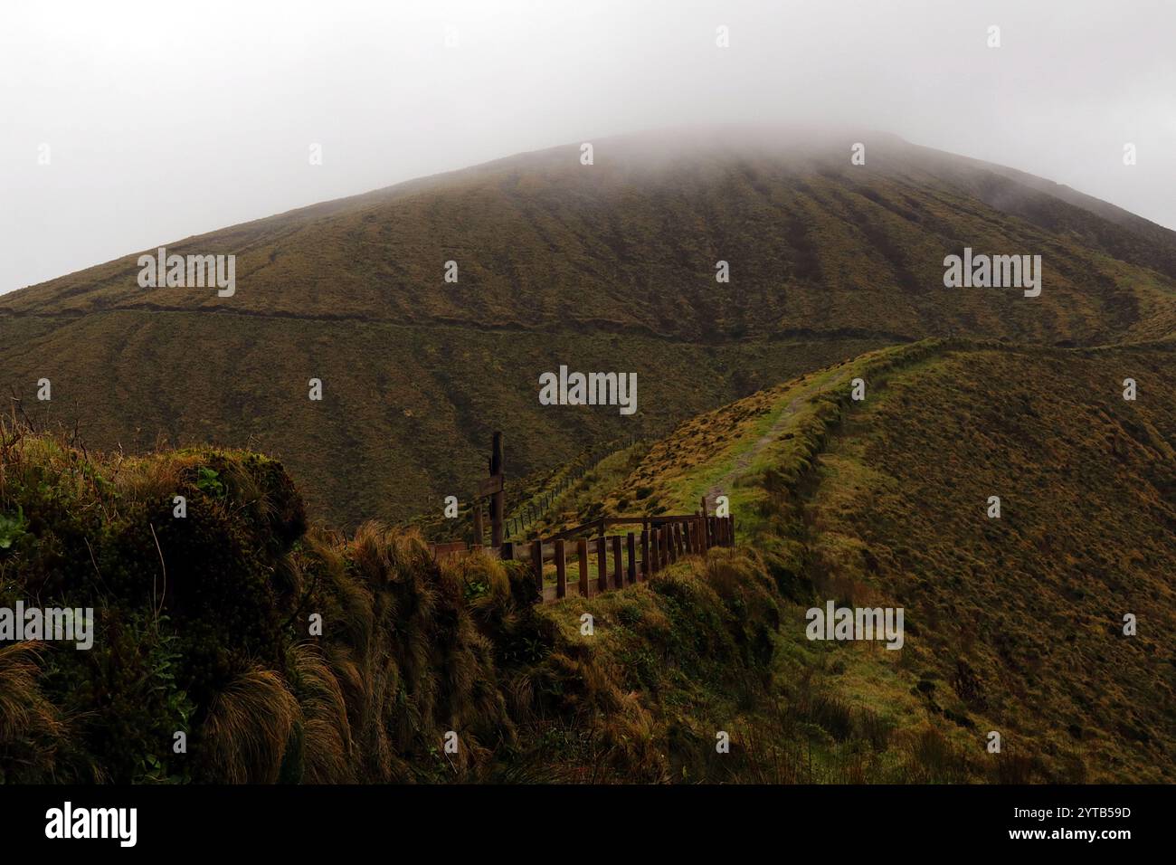 Un sentiero panoramico si snoda lungo la cima della nebbiosa cima Caldeira nelle Azzorre, invitando gli avventurieri ad esplorare paesaggi lussureggianti e panorami mozzafiato Foto Stock
