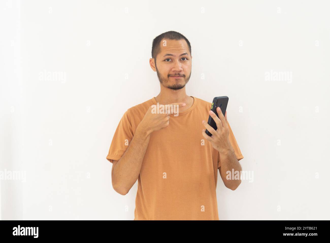 I giovani uomini che indossano una camicia arancione puntano al sorriso del telefono mobile su sfondo bianco isolato Foto Stock
