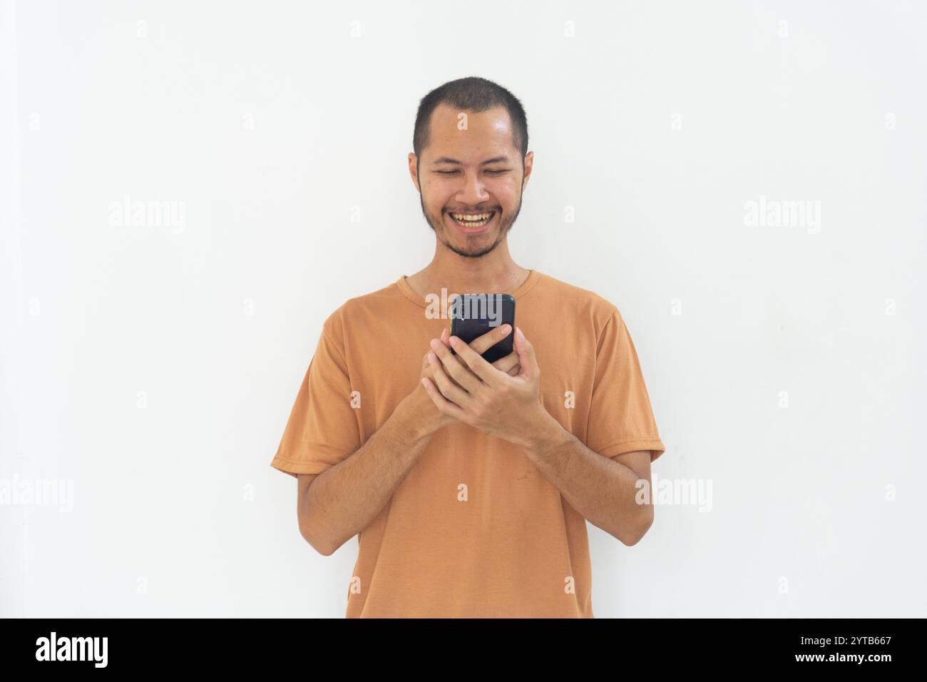 I giovani uomini che indossano una camicia arancione sorridono utilizzando il telefono cellulare su sfondo bianco isolato Foto Stock
