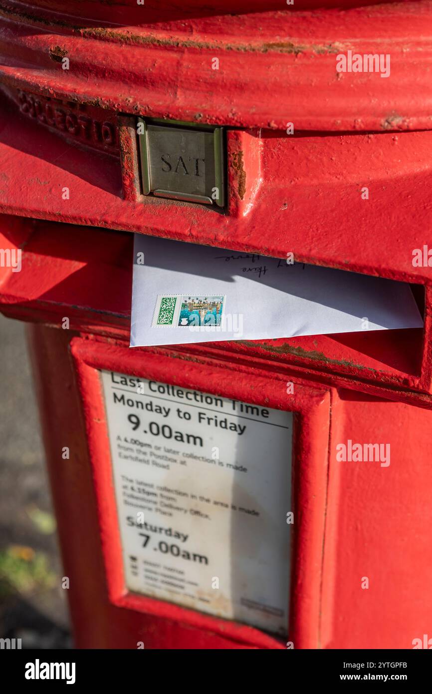 Un biglietto di Natale con un francobollo natalizio in una scatola rossa di lettere inglesi Foto Stock