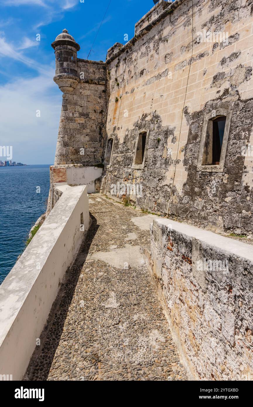 Un muro di pietra con un sentiero che conduce ad esso. Il muro è bianco e il sentiero è fatto di pietre. La vista dell'oceano è sullo sfondo Foto Stock