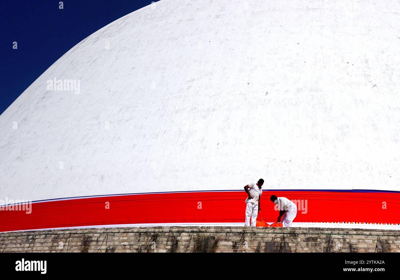 I devoti preparano un vivace tessuto rosso alla base dell'iconico Ruwanwelisaya Stupa ad Anuradhapura, Sri Lanka, simboleggiando fede e tradizione. Foto Stock