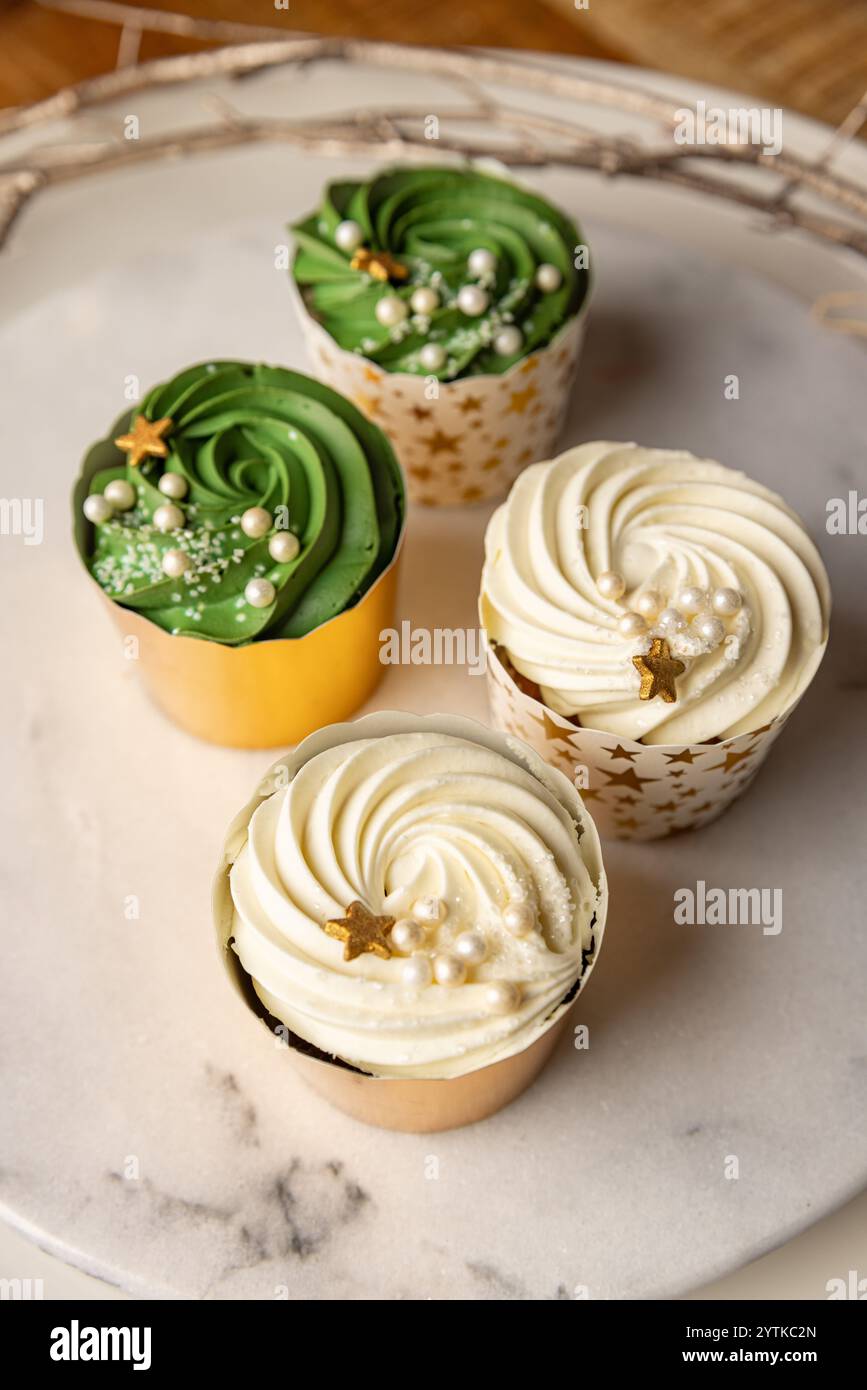 Quattro cupcake, due con glassa verde e due con glassa bianca, decorati con stelle dorate e spruzzi bianchi, si siedono su un vassoio di marmo Foto Stock