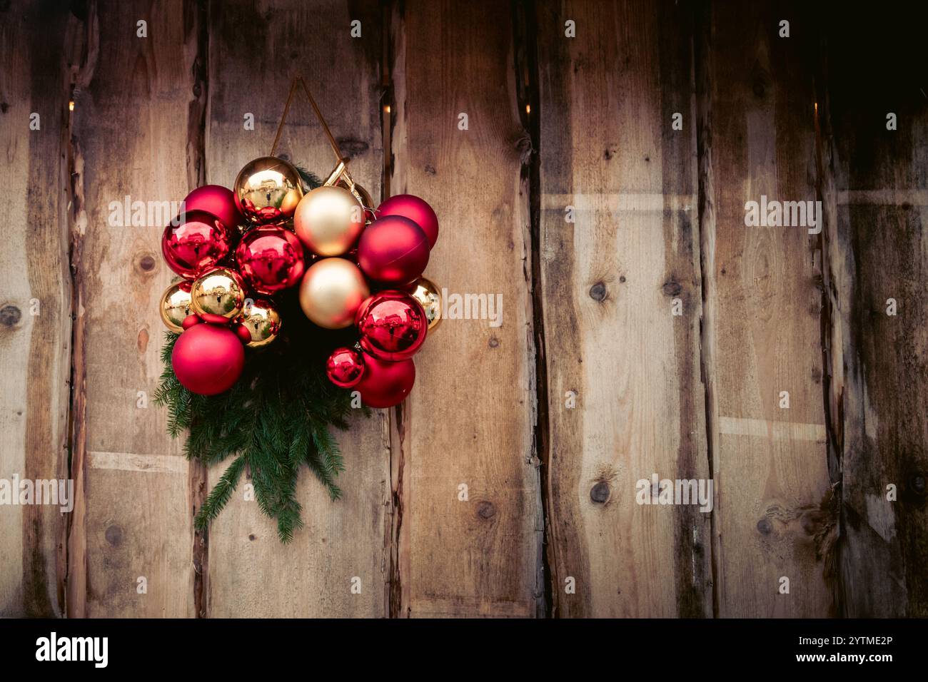 Corona di Natale con ornamenti rossi e dorati su fondo in legno rustico. Foto di alta qualità Foto Stock