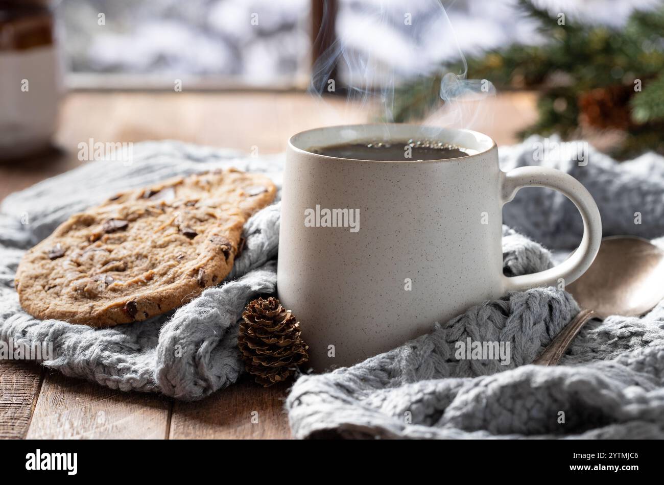 Tazza di caffè al vapore e coperta vicino a una finestra con sfondo invernale innevato Foto Stock