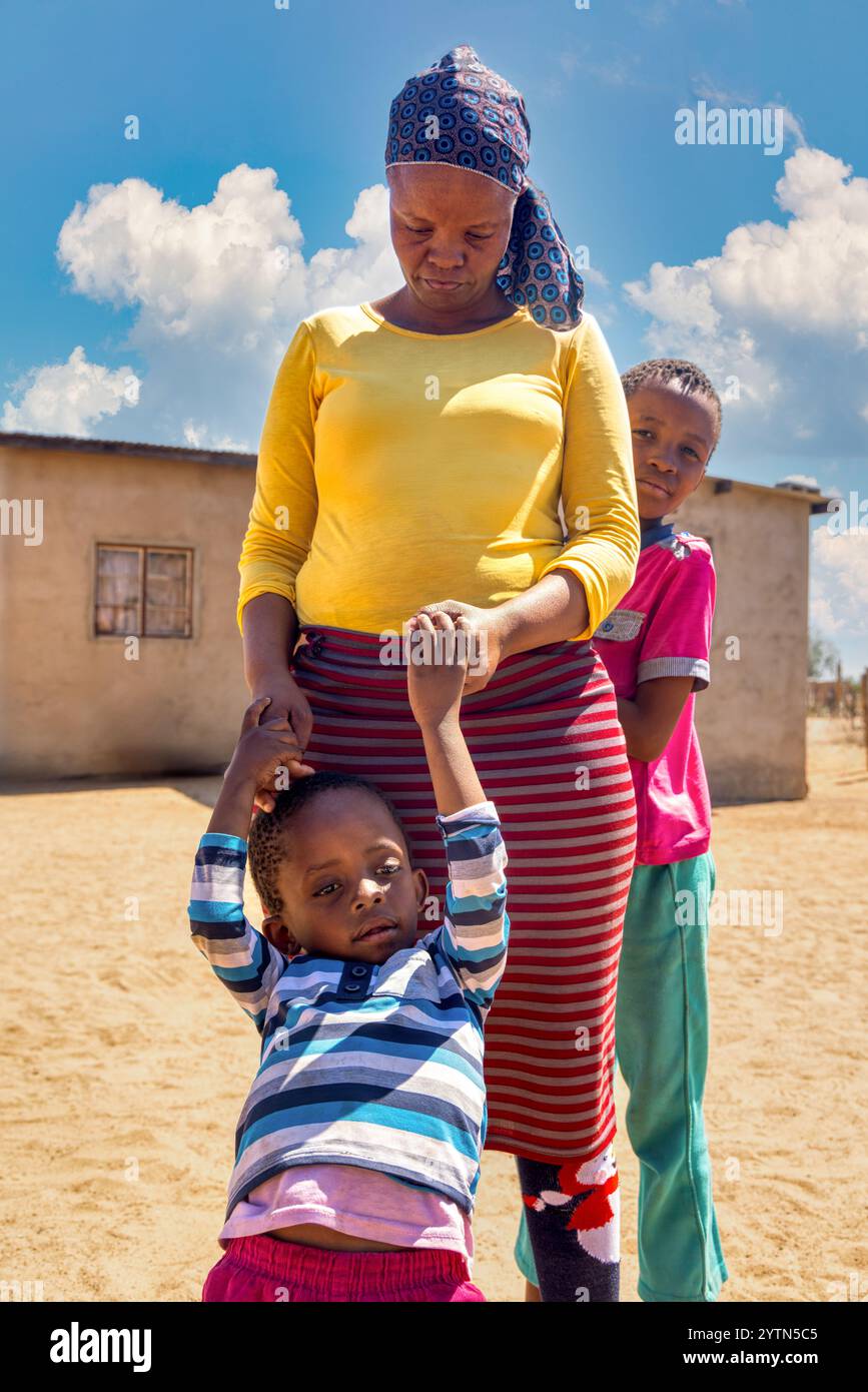 villaggio africano, donna, famiglia madre e figli, in piedi davanti alla casa nel cortile Foto Stock