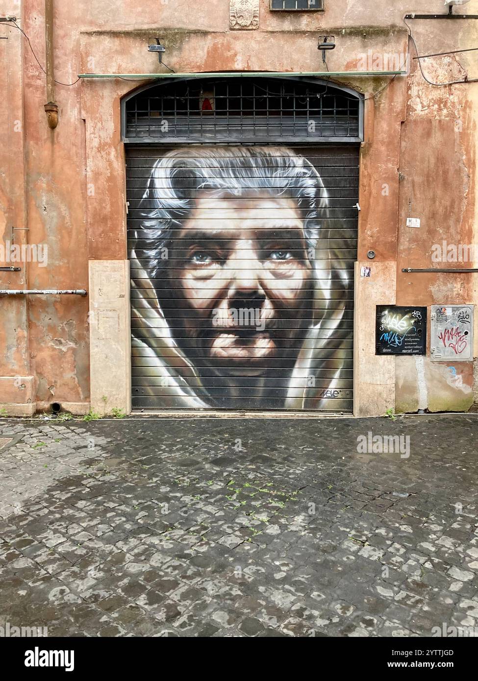 Un ritratto di uno spray facciale di una donna anziana dipinto su una porta con persiane di metallo dall'artista di strada neve nella zona di Trastevere a Roma - Immagine stock catturata con smartphone