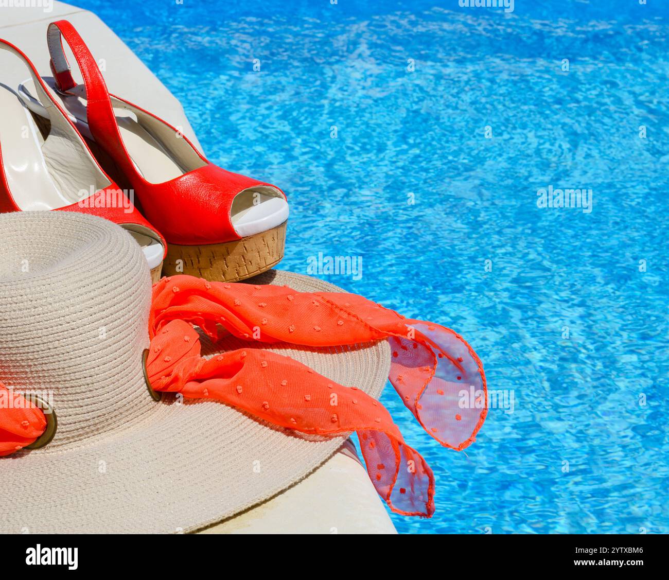 Cappello e sandali da donna accanto alla piscina. Bellissimi sandali rossi e paglia su uno sfondo di acqua blu Foto Stock