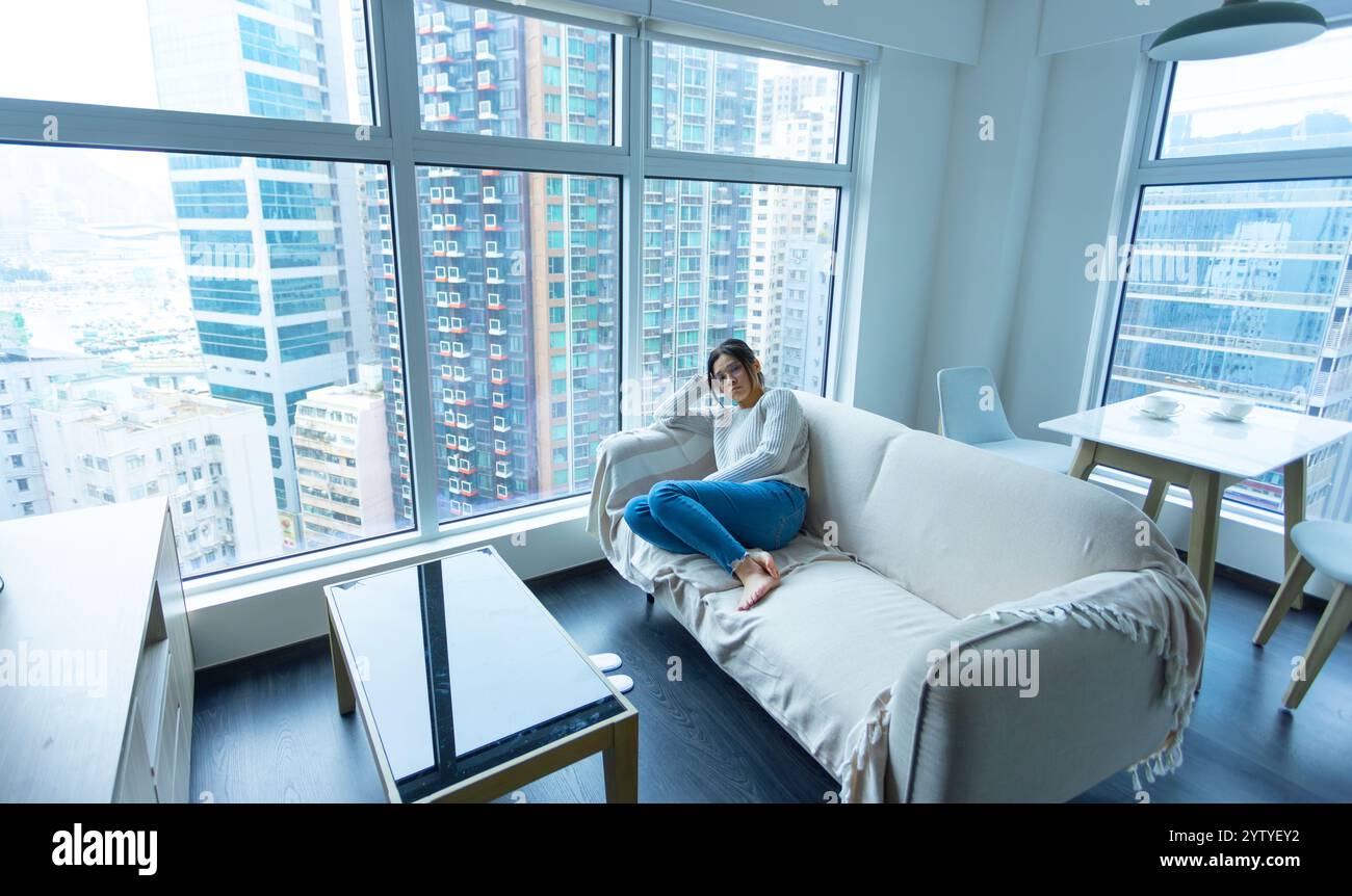 la donna indossa gli occhiali seduti sul divano e si sente stressata, scattata a tutto il corpo con lo sfondo della casa Foto Stock