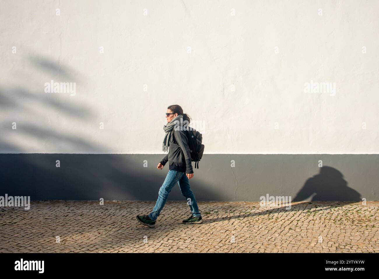 donna con uno zaino che cammina accanto a un muro bianco, esercizio fisico. Foto Stock