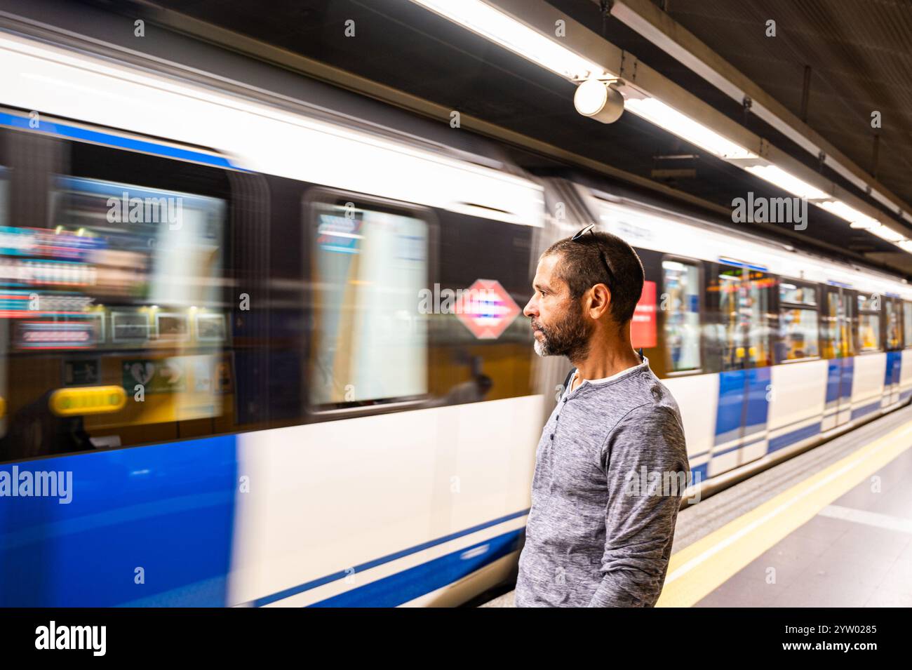 Un uomo sta su una piattaforma della metropolitana, a guardare un treno che passa. Il treno si sta muovendo velocemente e l'uomo ha fretta Foto Stock