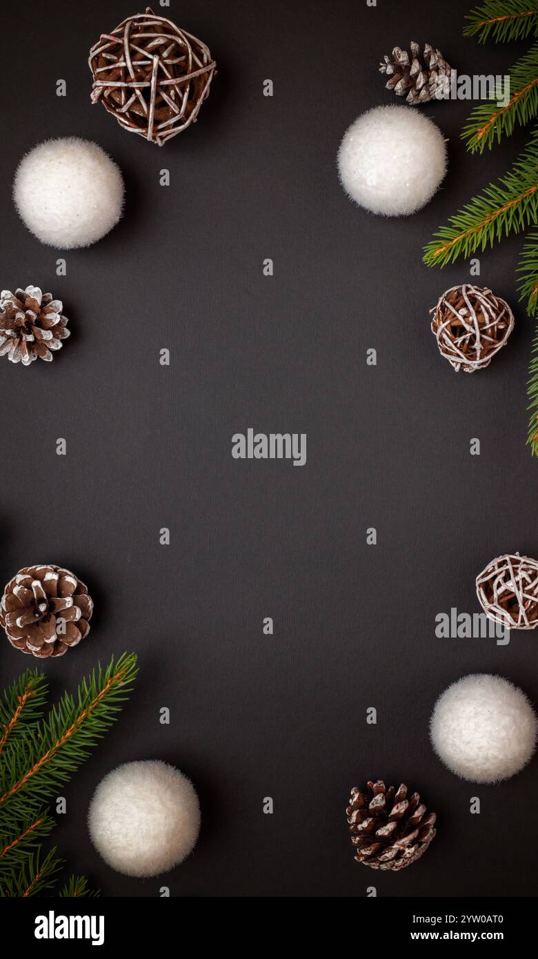 Vista dall'alto, decori di Natale su sfondo nero, circondati da ornamenti bianchi, rami di abete e pineconi, con spazio centrale Foto Stock
