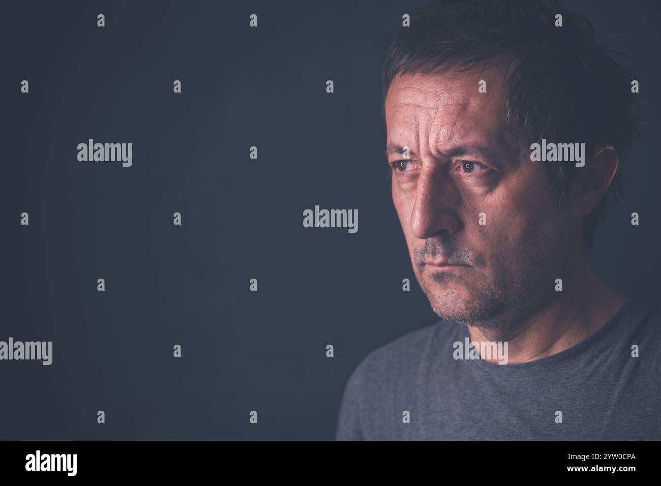 Ritratto di un uomo medio adulto, serio e casual, che indossa una camicia grigia in camera buia, messa a fuoco selettiva Foto Stock