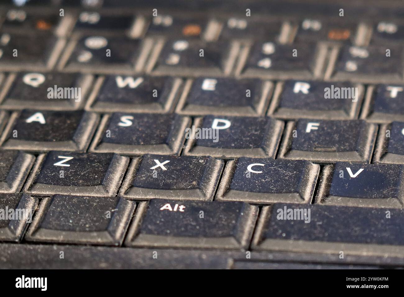 Una vista ravvicinata di una tastiera usurata rivela segni di utilizzo intensivo. Polvere e sporcizia accumulati sui tasti suggeriscono frequenti sessioni di digitazione. La b Foto Stock