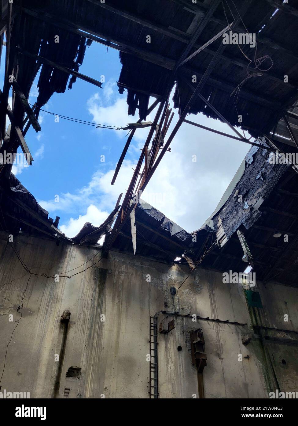 Tetto industriale danneggiato che espone cielo e caratteristiche strutturali intemperie - Immagine stock catturata con smartphone