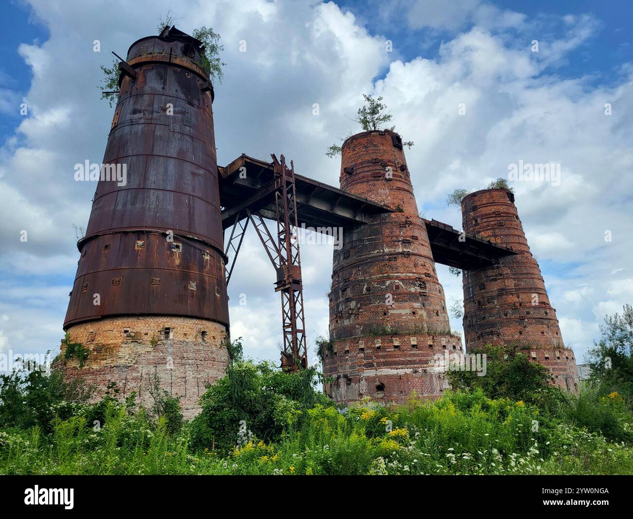 Rustiche torri industriali abbandonate nel paesaggio verde sovrastato sotto il cielo blu Foto Stock