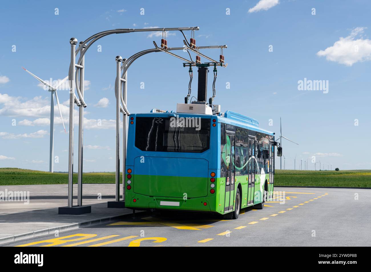 L'autobus elettrico alla fermata è caricato dal pantografo. Turbine eoliche all'orizzonte. Foto Stock