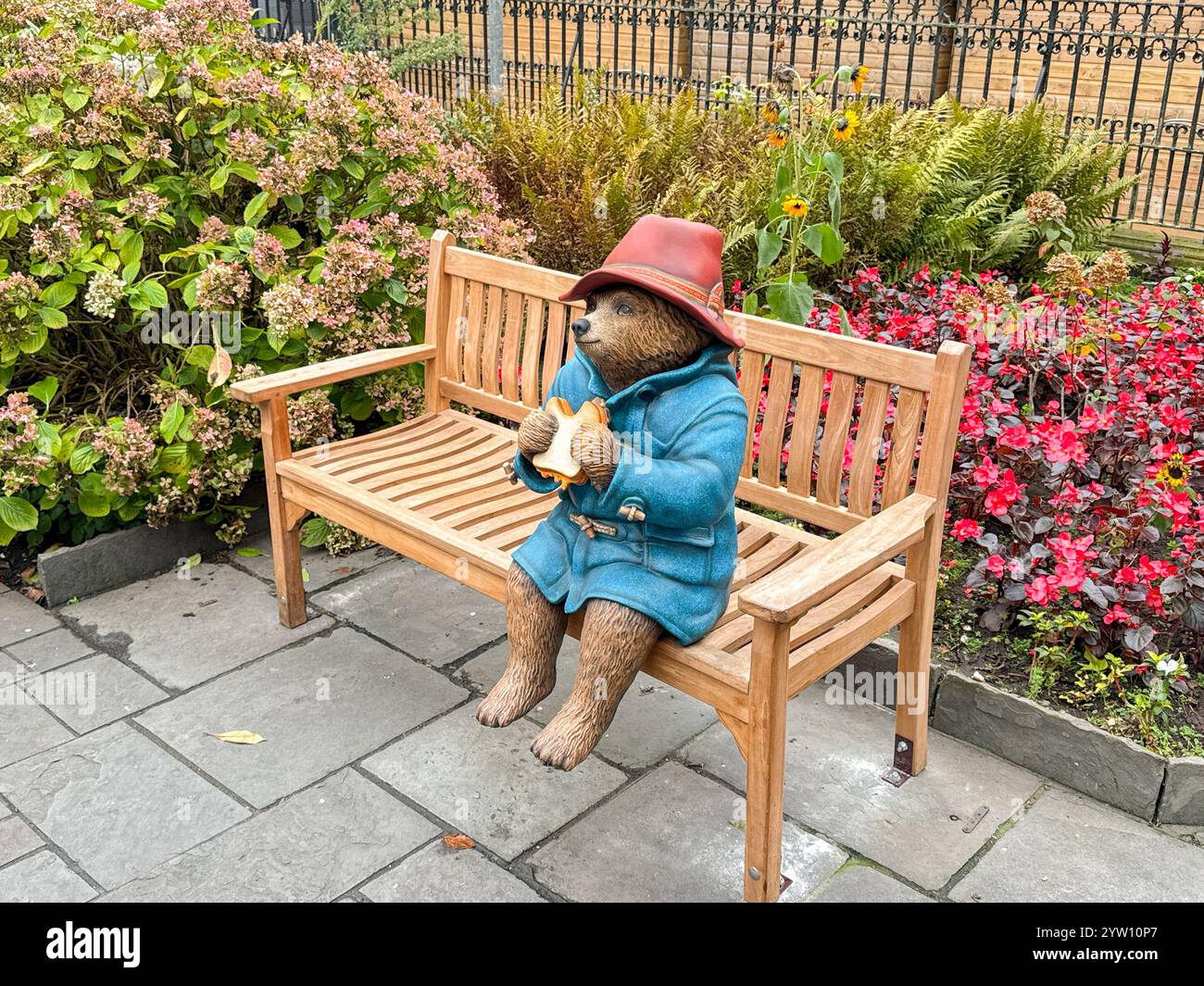 Cardiff, Galles - 10 novembre 2024: Modello di orso Paddington seduto su una panchina di legno in un parco pubblico nel centro di Cardiff - Immagine stock catturata con smartphone