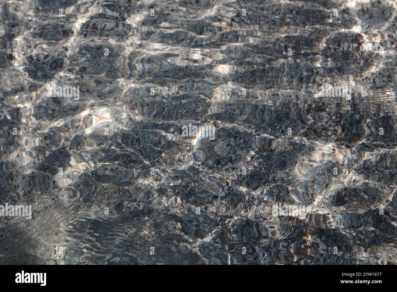 Una tranquilla cattura della consistenza dell'acqua in un lago, che mostra morbide increspature e riflessi di luce scintillanti. Le piccole onde creano un ambiente dinamico ma rilassante. Foto Stock