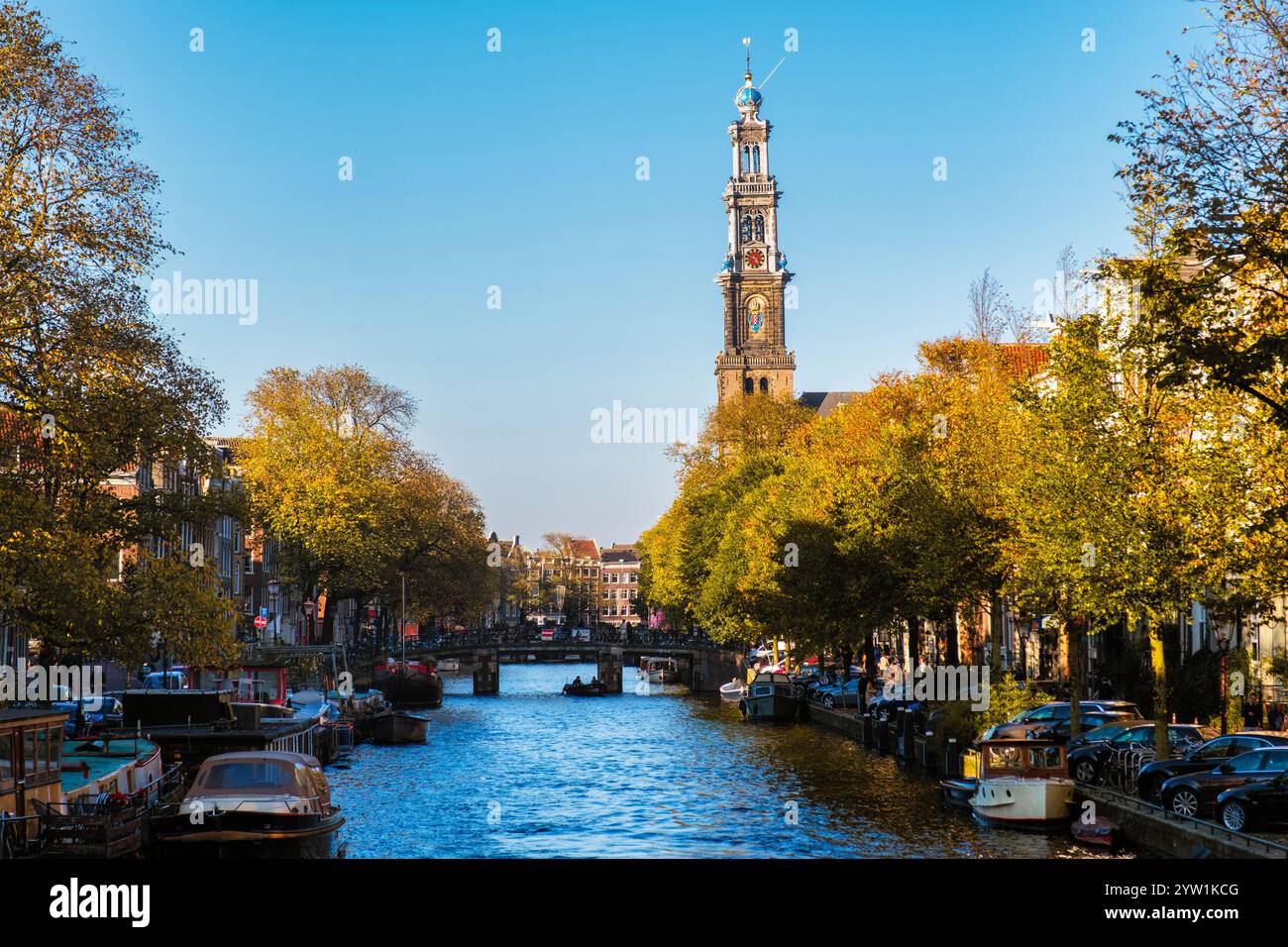 Le foglie d'oro scendono dolcemente dagli alberi lungo i canali di Amsterdam. L'iconica torre di Westerkerk si erge alta mentre le barche galleggiano pacificamente, captur Foto Stock