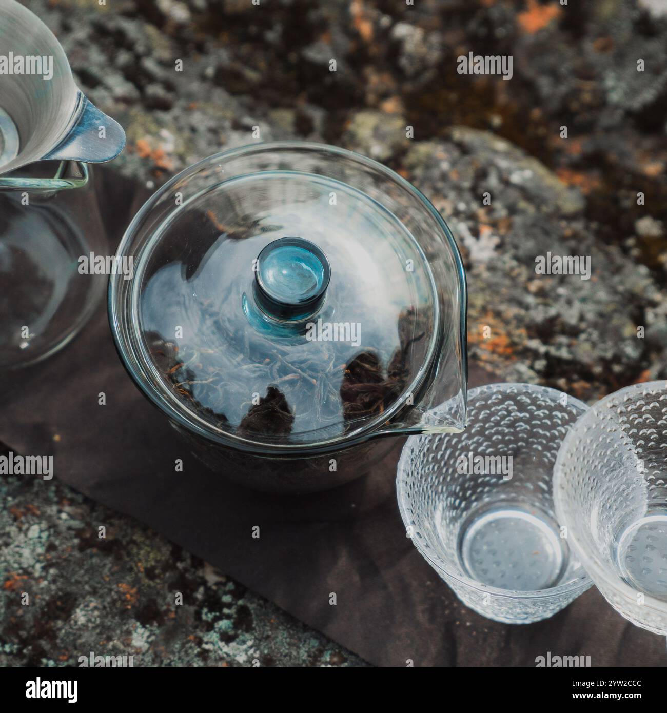 Un set per il tè dallo stile splendido che mette in mostra una squisita teiera di vetro insieme a eleganti tazze posizionate sulla pietra testurizzata Foto Stock