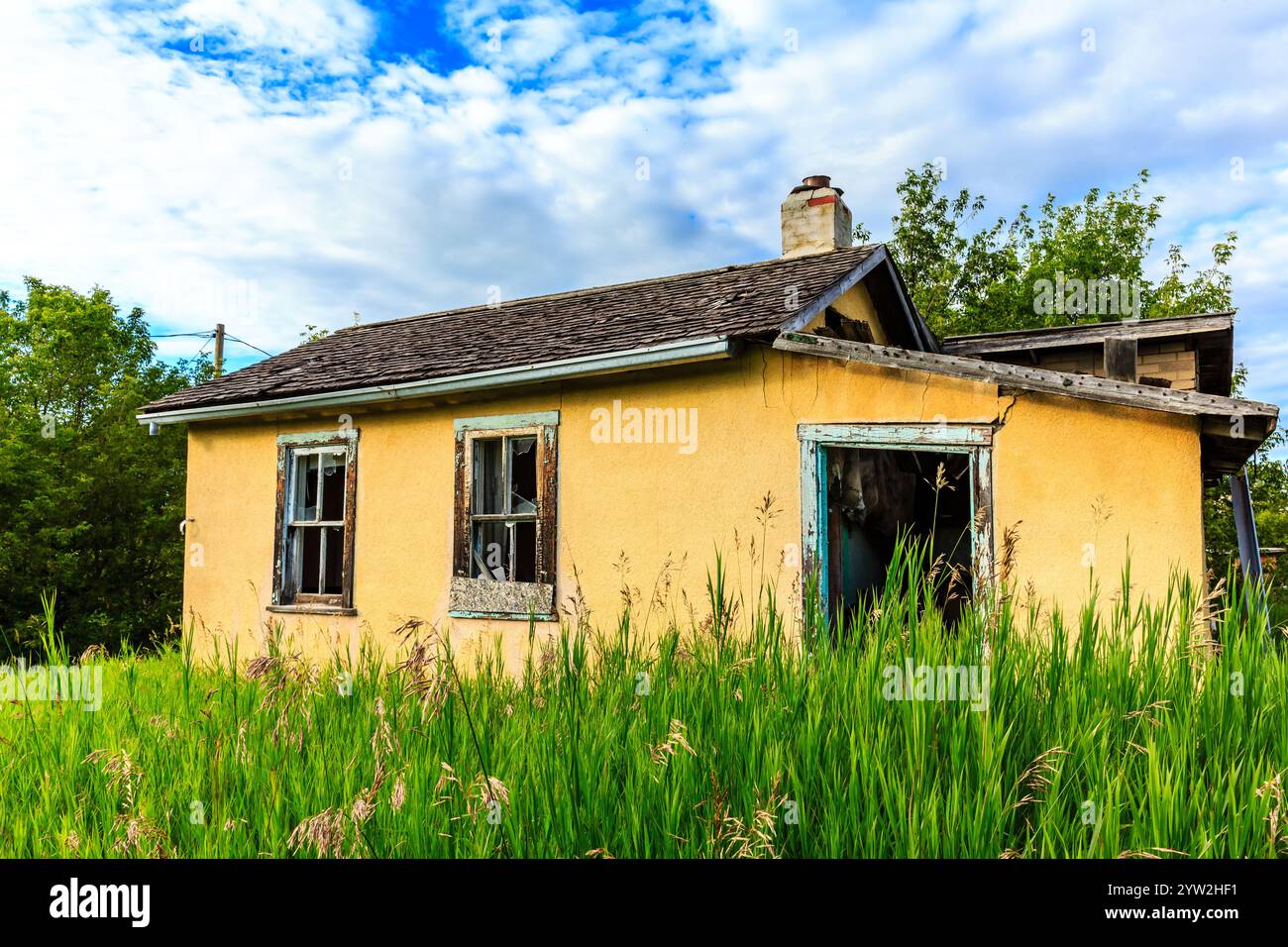 Una piccola casa gialla con un camino e una finestra. La casa è circondata da erba alta Foto Stock