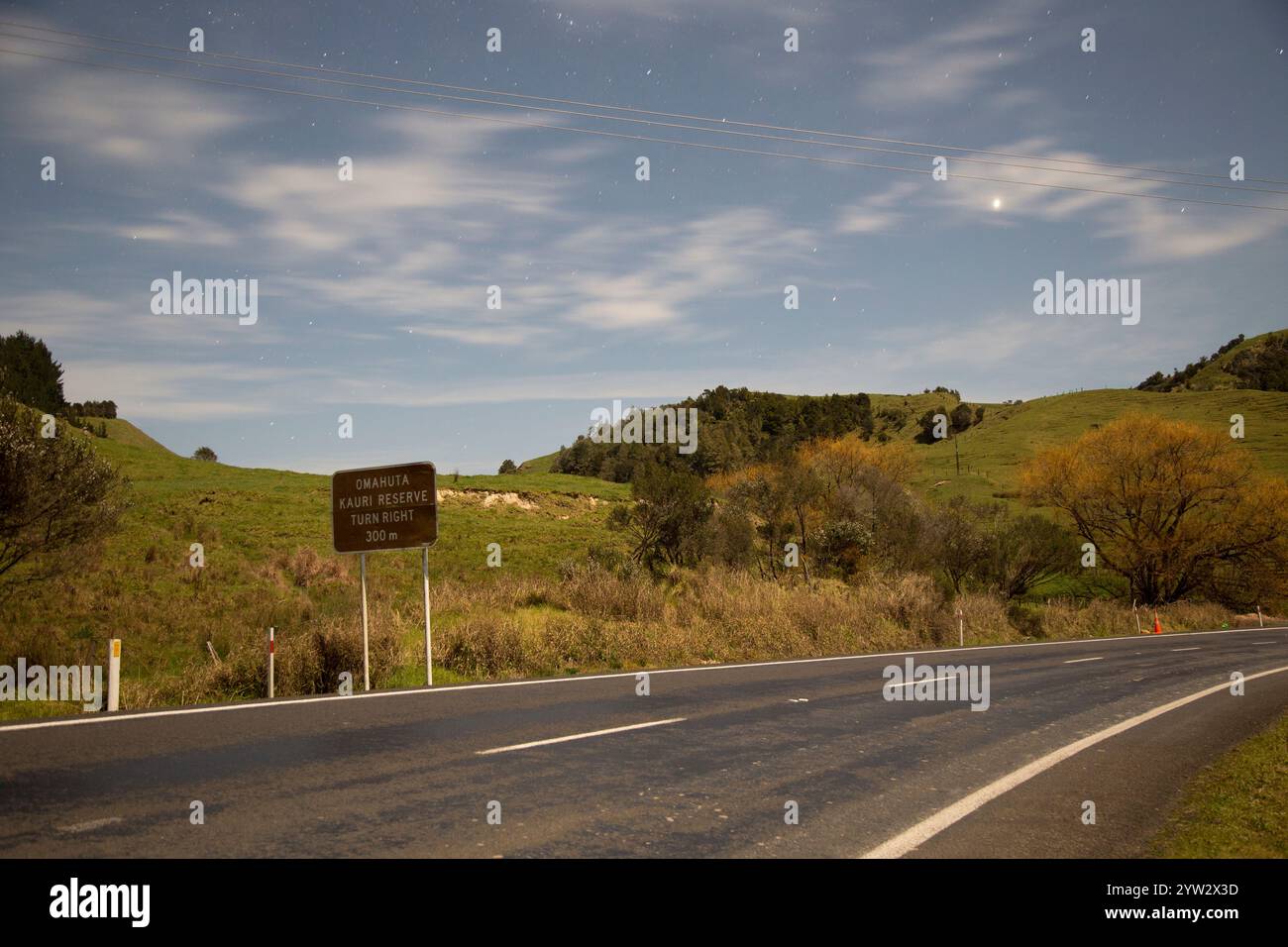 Paesaggio notturno di una strada tortuosa con un cartello che indica una vicina riserva di catena e pecore che pascolano sotto un cielo stellato, Northland, nuova Zelanda Foto Stock