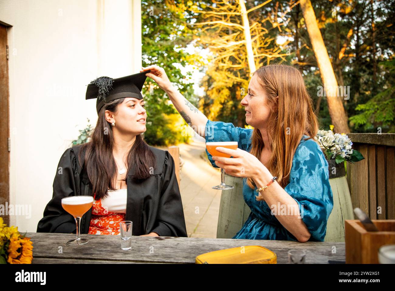 Orgogliosa madre che regola il cappello di laurea di sua figlia mentre si godono un drink celebrativo a un tavolo all'aperto, Bournemouth, Dorset UK Foto Stock