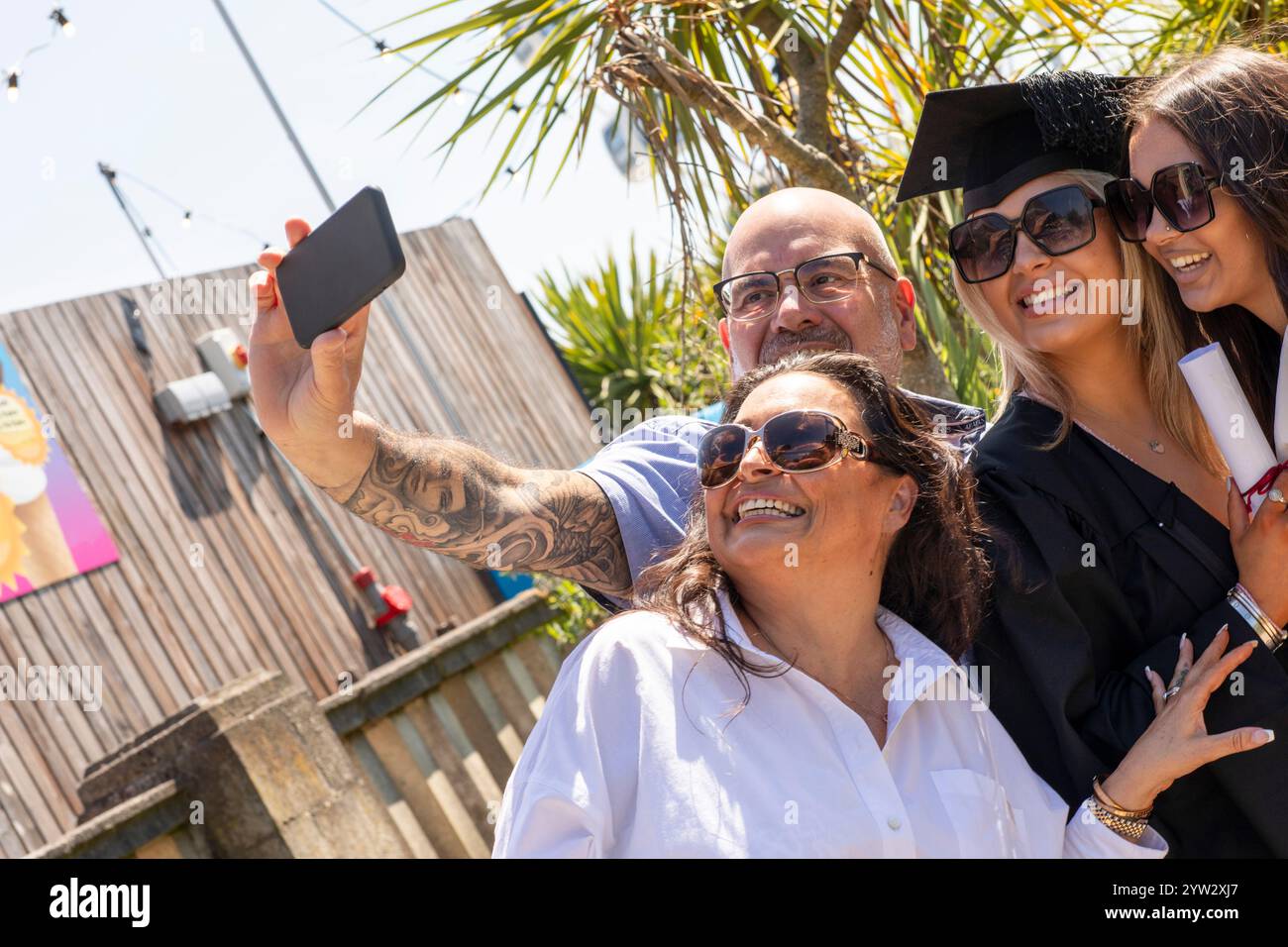 Un gioioso gruppo di quattro persone che scattano un selfie in una giornata di sole, con due persone in copricapo per celebrare una pietra miliare, Bournemouth, Dorset UK Foto Stock