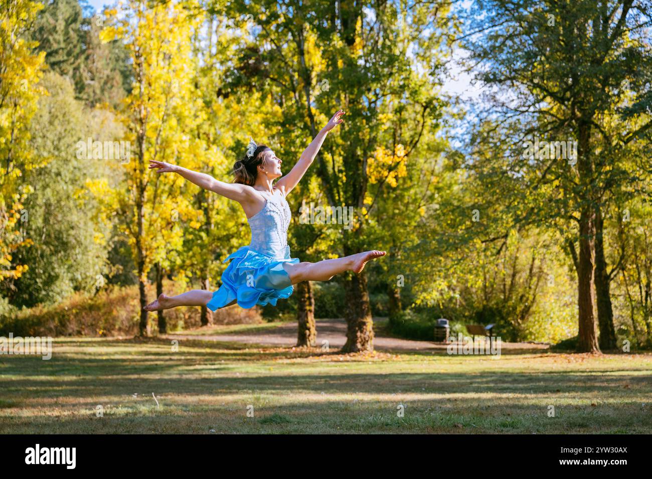 Gioiosa ballerina che danzava all'aperto in un parco con alberi autunnali sullo sfondo. Foto Stock