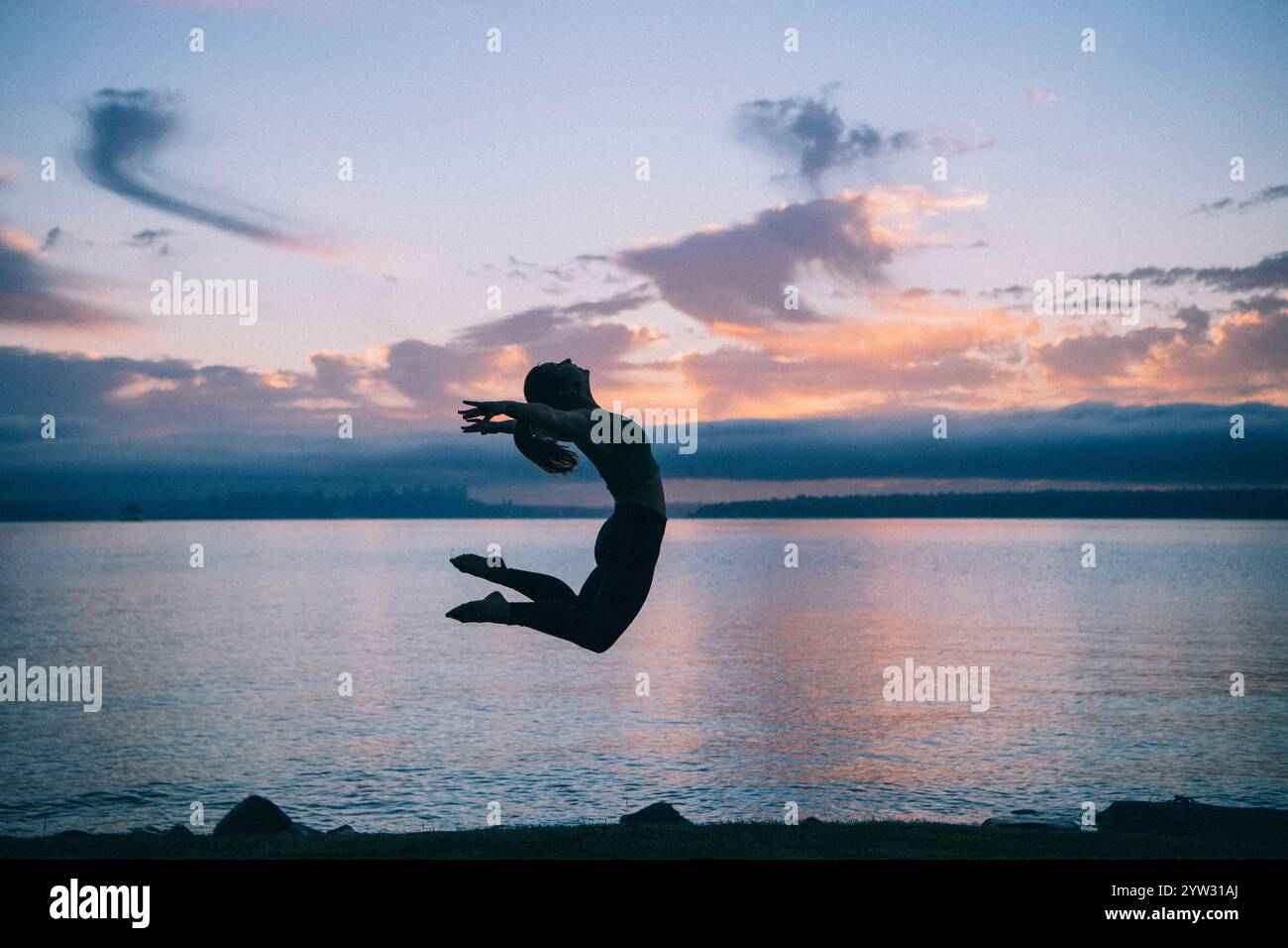 Silhouette di una donna che salta sul lungolago al tramonto con nuvole nel cielo. Foto Stock