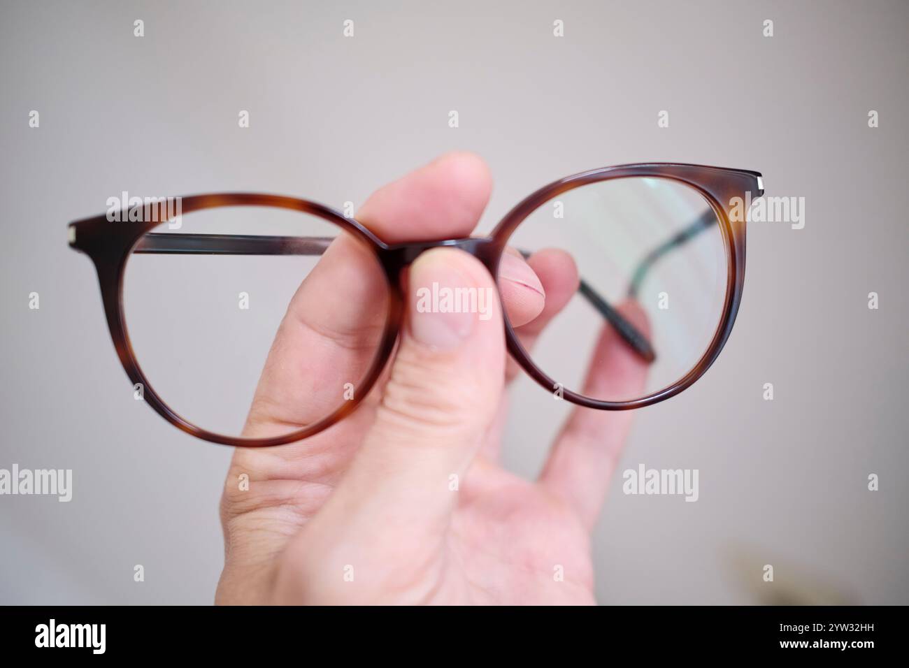 Primo piano di una persona che tiene un paio di occhiali da vista marroni su uno sfondo sfocato. Foto Stock