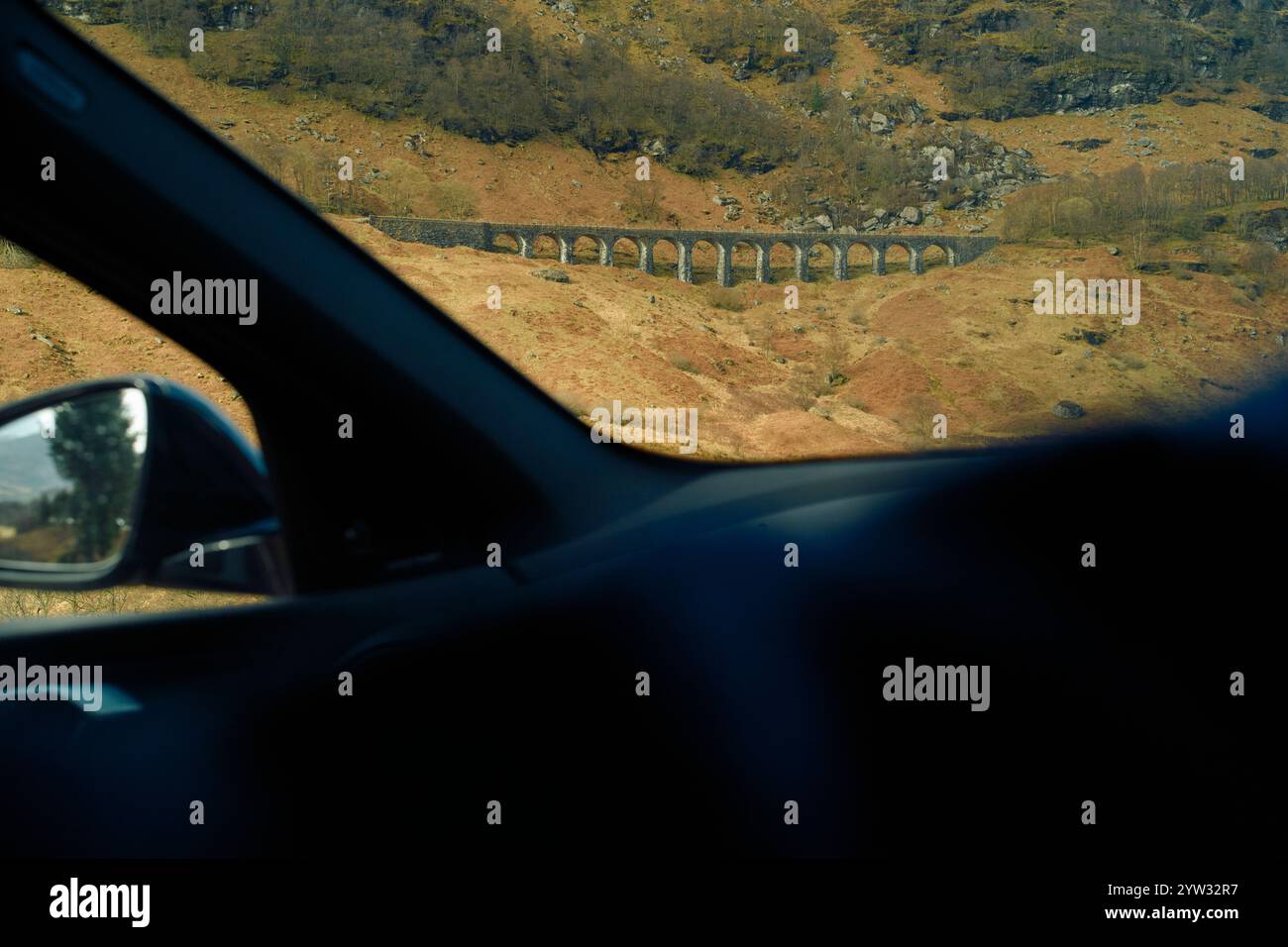 Vista di un antico ponte di pietra attraverso un finestrino incorniciato dall'interno del veicolo sullo sfondo di terreni accidentati, Highlands, Scozia Foto Stock
