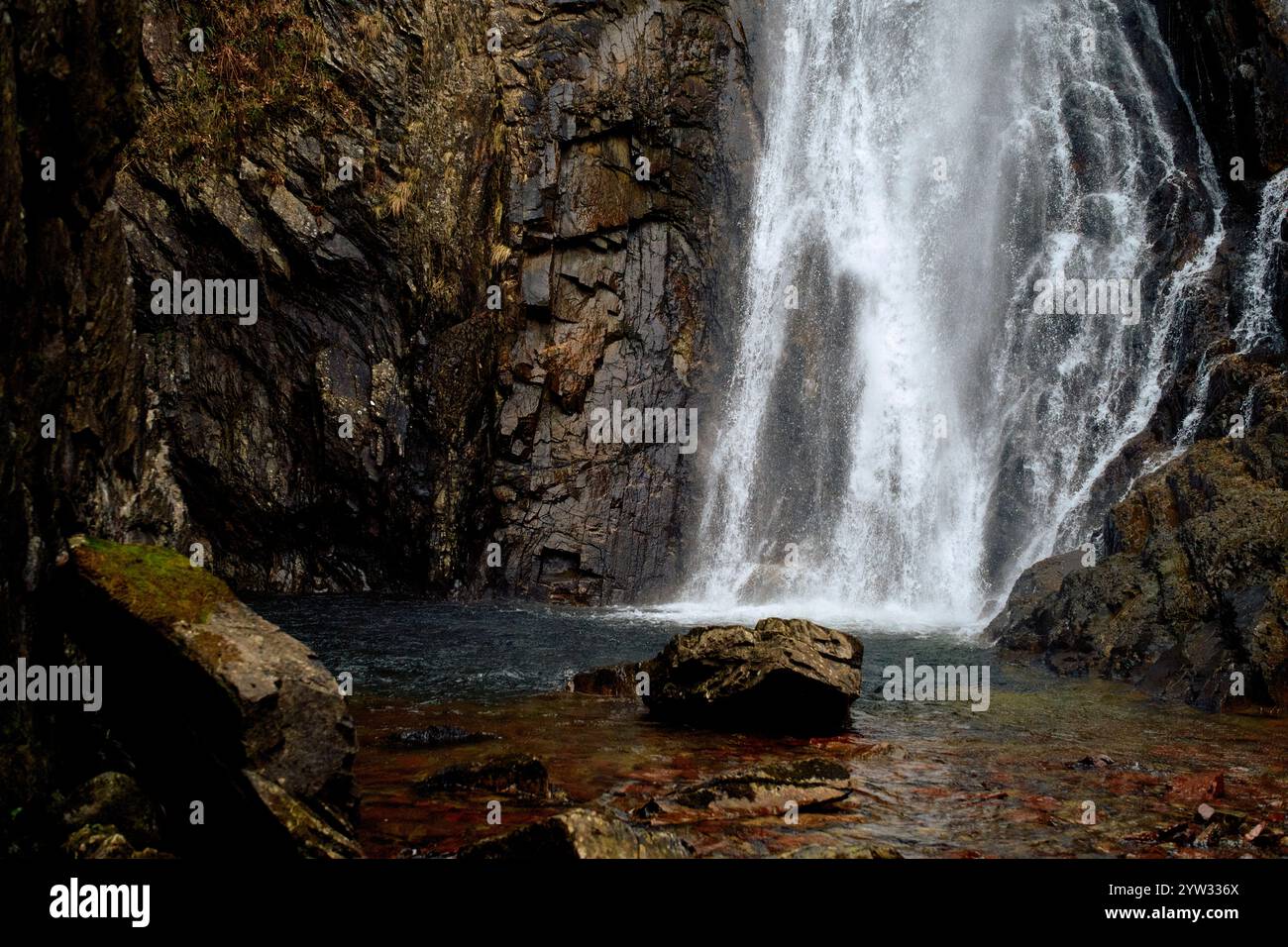Cascata che si tuffa in una tranquilla piscina circondata da aspre pareti rocciose e fogliame di colore autunnale, Scozia Foto Stock
