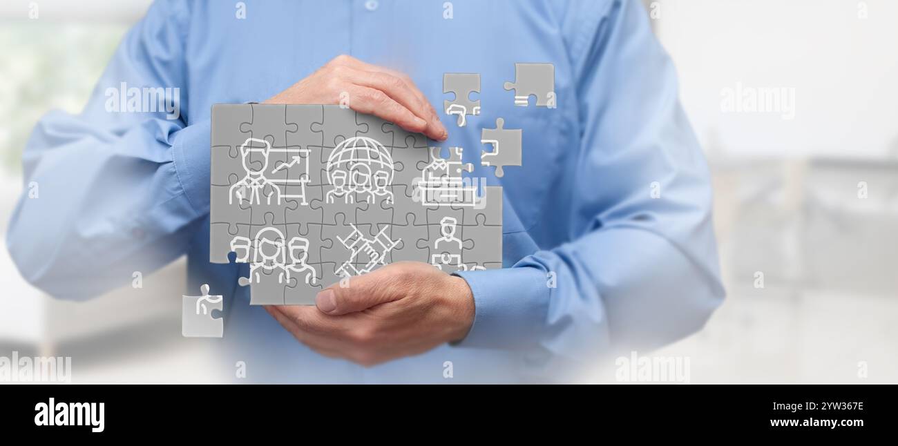 Un uomo d'affari con una camicia blu ha un puzzle digitale con varie icone legate al business. L'immagine rappresenta il lavoro di squadra, la strategia e i planni di business Foto Stock