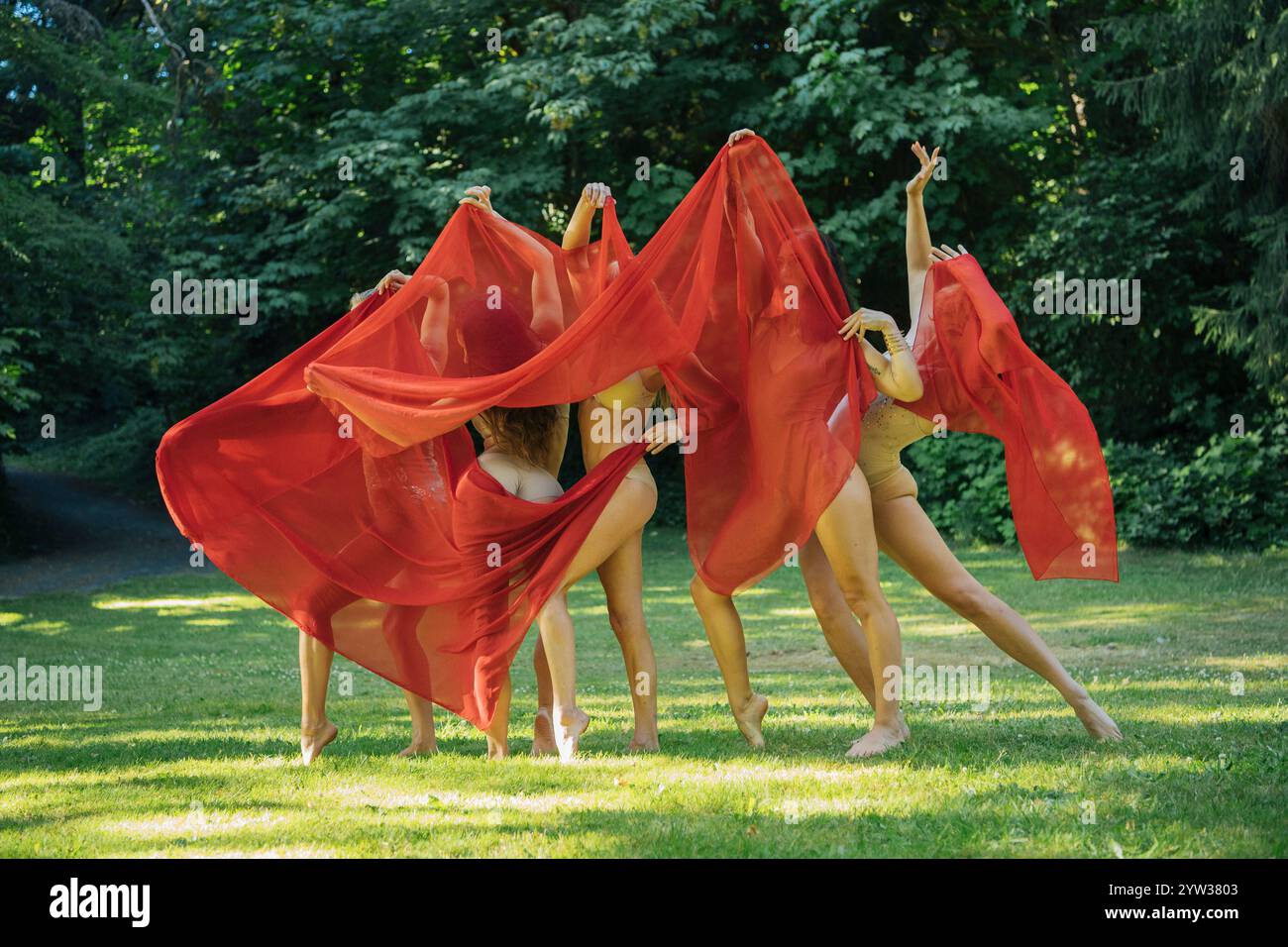 Cinque ballerini in tessuto rosso eseguono una danza espressiva in un parco illuminato dal sole, negli Stati Uniti Foto Stock