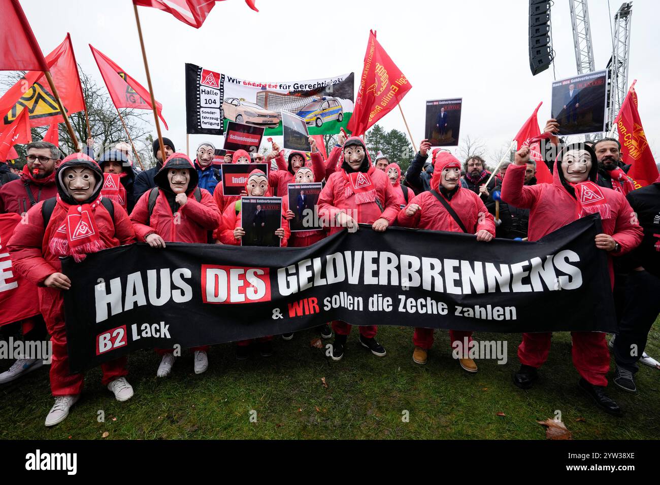 Wolfsburg, Germania. 9 dicembre 2024. I dipendenti VW partecipano a un rally IG Metall di fronte alla sede centrale della Volkswagen durante uno sciopero di avvertimento nello stabilimento principale della casa automobilistica tedesca di Wolfsburg. Lo striscione recita: "Casa dei soldi in fiamme e dovremmo pagare il conto!" Credito: Martin Meissner/AP POOL/dpa/Alamy Live News Foto Stock