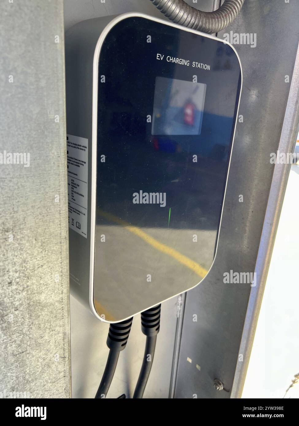 Primo piano dell'interfaccia digitale di una stazione di ricarica EV, che riflette l'ambiente urbano circostante. Foto Stock