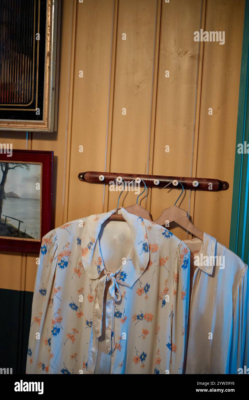 Una blusa floreale e una camicia bianca unita appesa a un appendiabiti in legno vintage su una parete gialla e turchese, Trondheim, Norvegia Foto Stock