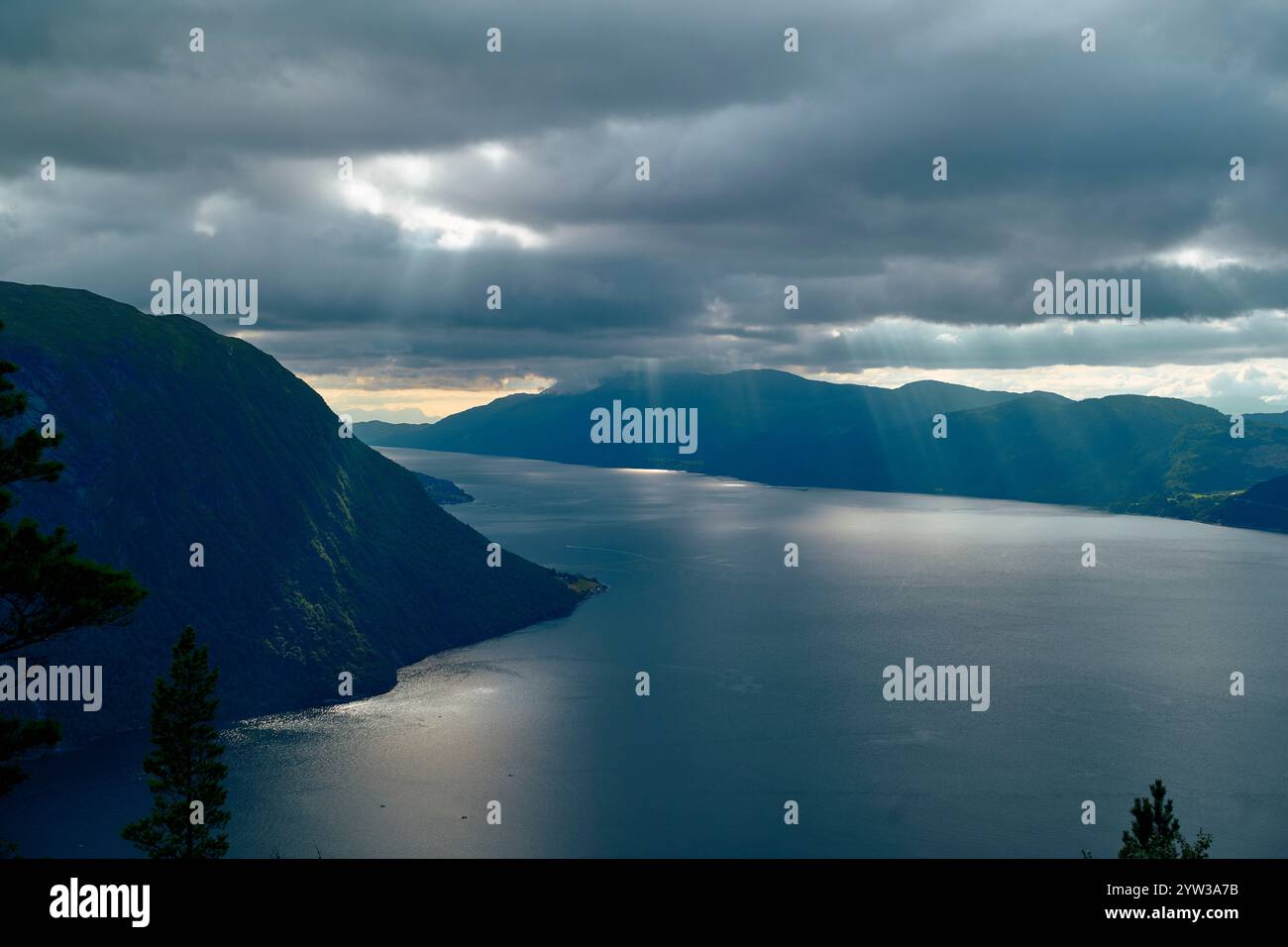 I raggi del sole si infrangono attraverso nuvole scure su un tranquillo fiordo circondato da ripide montagne, Romsdalfjorden, Norvegia Foto Stock