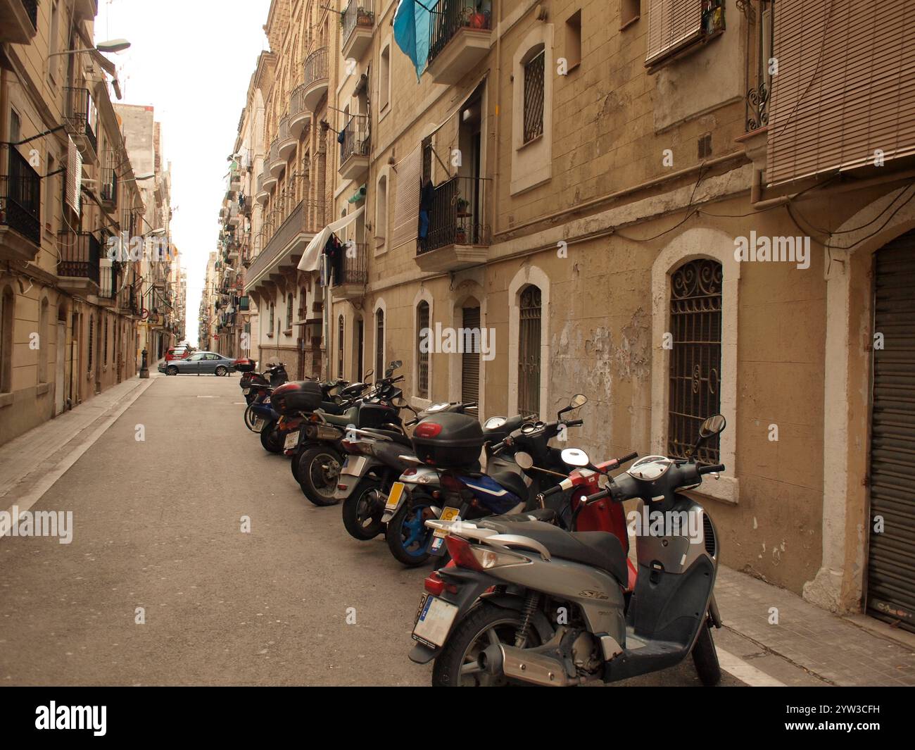 Una strada stretta costeggiata da motociclette parcheggiate sul marciapiede e classici condomini con balconi in una città europea, Barcellona, Spagna Foto Stock