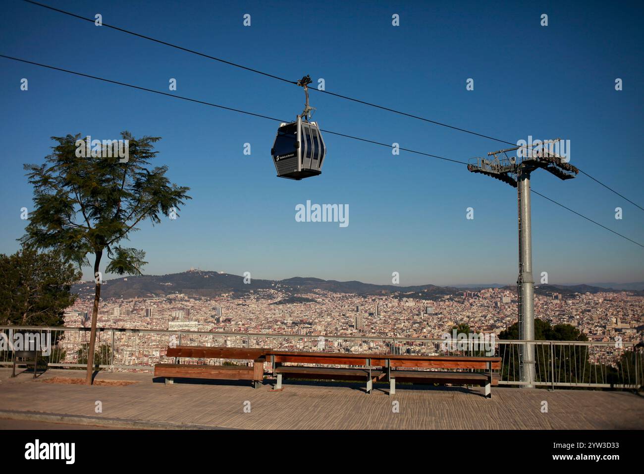Funivia sopra un paesaggio urbano panoramico con un cielo azzurro e una panchina in primo piano, Barcellona, Spagna Foto Stock