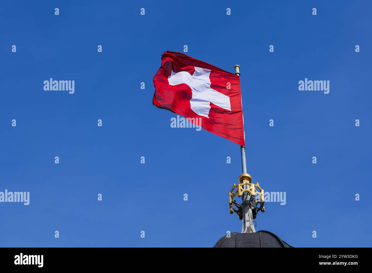 La bandiera nazionale della Svizzera che soffia nel vento contro un cielo blu, bandiera svizzera in cima alla torre della chiesa di Grossmunster. Foto Stock